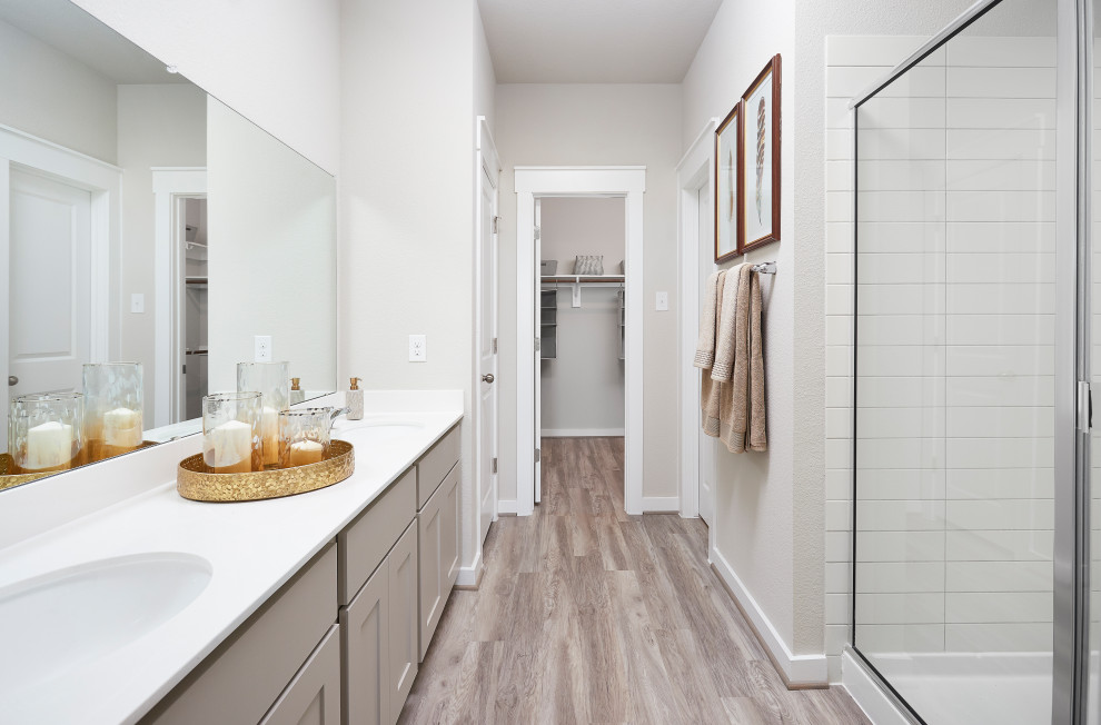 Photo of a medium sized contemporary ensuite bathroom in Austin with recessed-panel cabinets, beige cabinets, a corner shower, white tiles, ceramic tiles, light hardwood flooring, solid surface worktops, grey floors, a hinged door, white worktops, double sinks and a submerged sink.