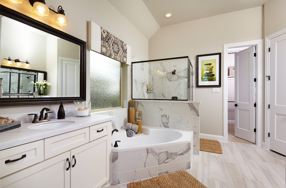 Photo of a large ensuite bathroom in Austin with recessed-panel cabinets, white cabinets, a corner bath, an alcove shower, beige tiles, ceramic tiles, beige walls, laminate floors, a submerged sink and limestone worktops.