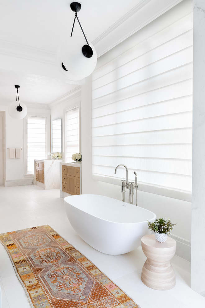 Modelo de cuarto de baño principal tradicional renovado grande con bañera exenta, paredes blancas, encimeras blancas, puertas de armario de madera clara y suelo blanco