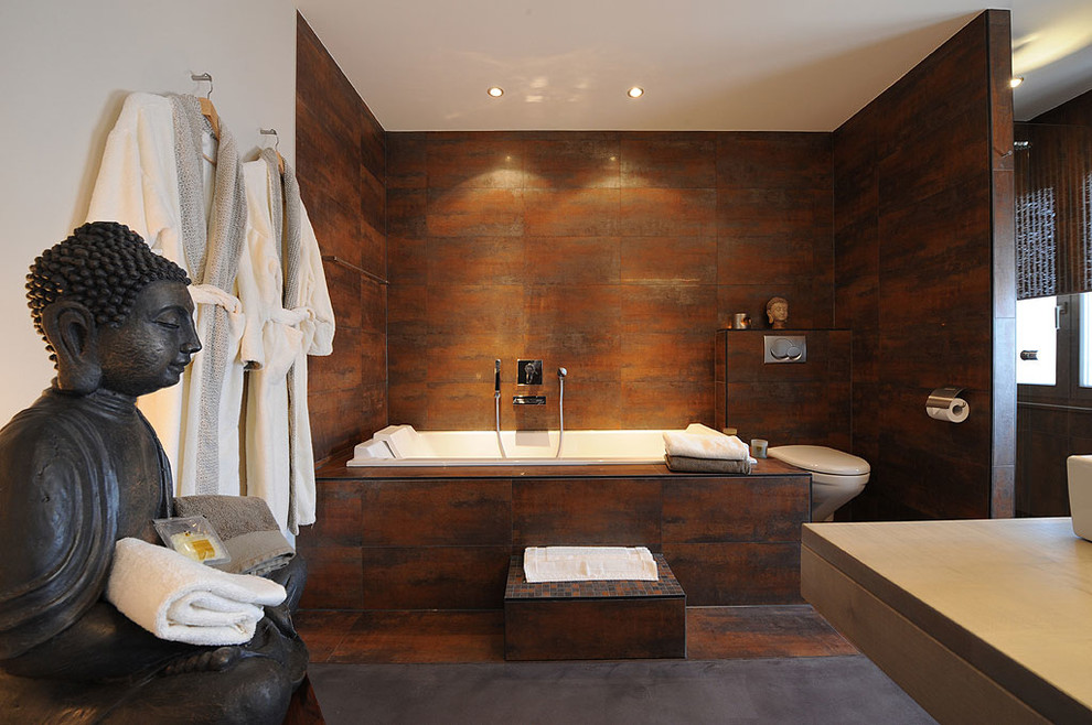 Inredning av ett asiatiskt en-suite badrum, med en vägghängd toalettstol, ett fristående handfat, en hörndusch, porslinskakel, vita väggar, betonggolv, brun kakel och ett platsbyggt badkar