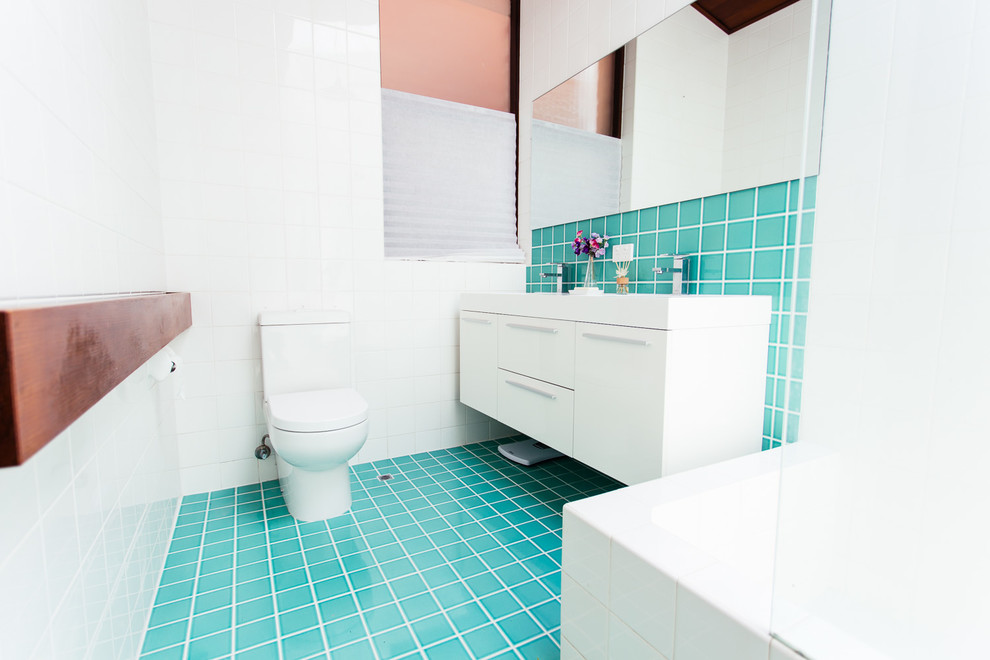 Exemple d'une salle d'eau exotique de taille moyenne avec un lavabo intégré, un placard à porte affleurante, des portes de placard blanches, un plan de toilette en surface solide, une baignoire d'angle, une douche d'angle, WC suspendus, un carrelage bleu, un carrelage en pâte de verre, un mur blanc et un sol en carrelage de céramique.