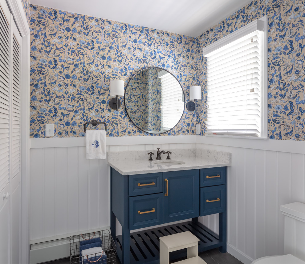 Cette photo montre une salle de bain bord de mer avec des portes de placard bleues, un mur multicolore, un lavabo encastré, un plan de toilette blanc et un placard avec porte à panneau encastré.