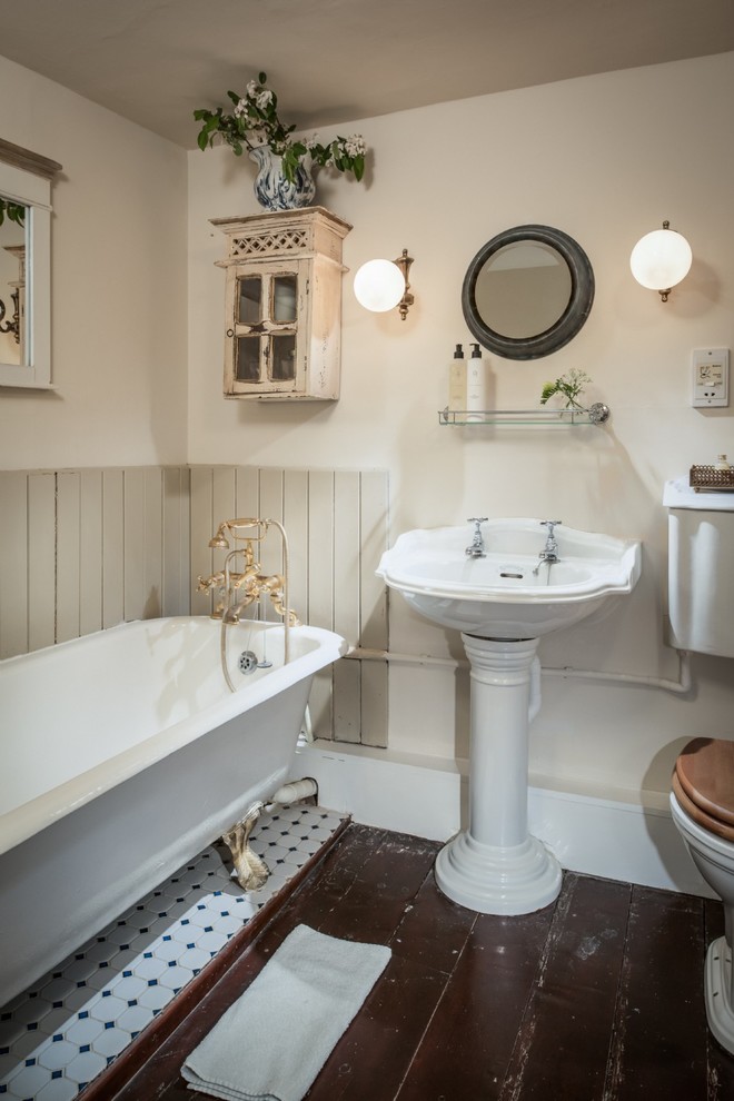 Inredning av ett klassiskt mellanstort badrum för barn, med ett badkar med tassar, en dusch/badkar-kombination, en toalettstol med separat cisternkåpa, vita väggar, mellanmörkt trägolv, ett piedestal handfat och brunt golv