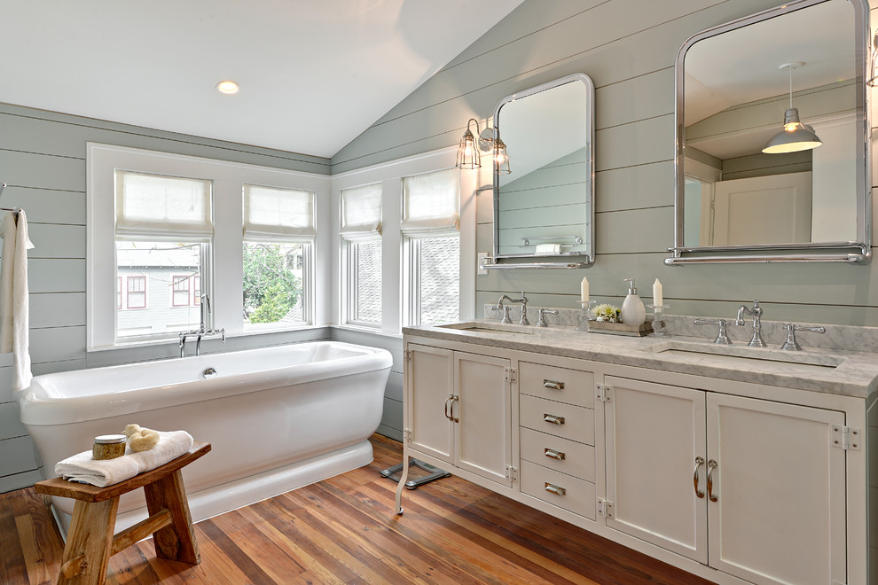 Transitional medium tone wood floor freestanding bathtub photo in Austin with an undermount sink, shaker cabinets, white cabinets, blue walls and marble countertops
