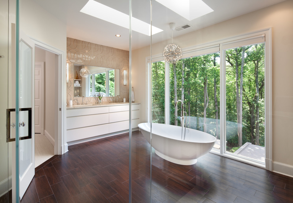 Modern inredning av ett stort en-suite badrum, med marmorbänkskiva, ett fristående badkar, en hörndusch, beige kakel, beige väggar, mörkt trägolv, släta luckor och vita skåp