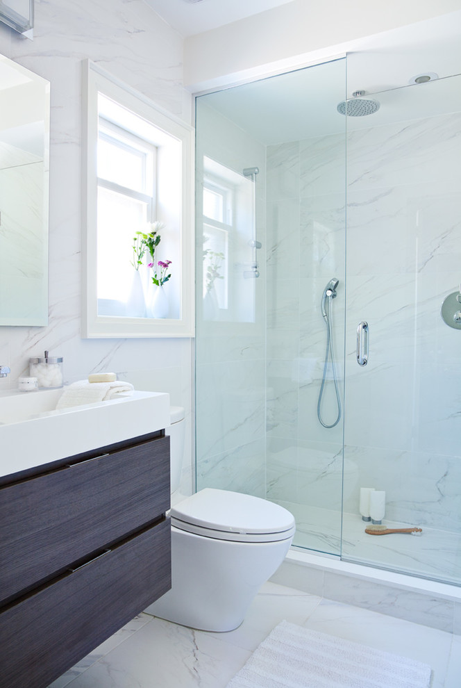 Источник вдохновения для домашнего уюта: ванная комната среднего размера в стиле модернизм с плоскими фасадами, серыми фасадами, душем в нише, унитазом-моноблоком, белой плиткой, мраморной плиткой, белыми стенами, мраморным полом, душевой кабиной, монолитной раковиной, столешницей из искусственного камня, белым полом и душем с распашными дверями