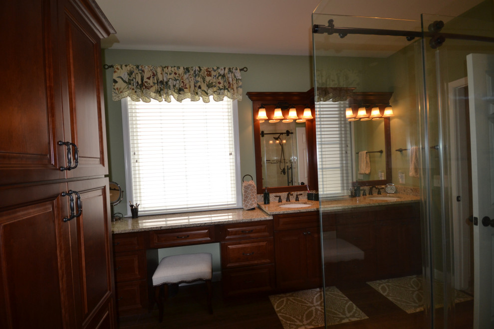 На фото: большая главная ванная комната в классическом стиле с фасадами с выступающей филенкой, фасадами цвета дерева среднего тона, угловым душем, унитазом-моноблоком, зелеными стенами, паркетным полом среднего тона, врезной раковиной, столешницей из гранита, коричневым полом, душем с раздвижными дверями, бежевой столешницей, нишей, тумбой под две раковины и встроенной тумбой