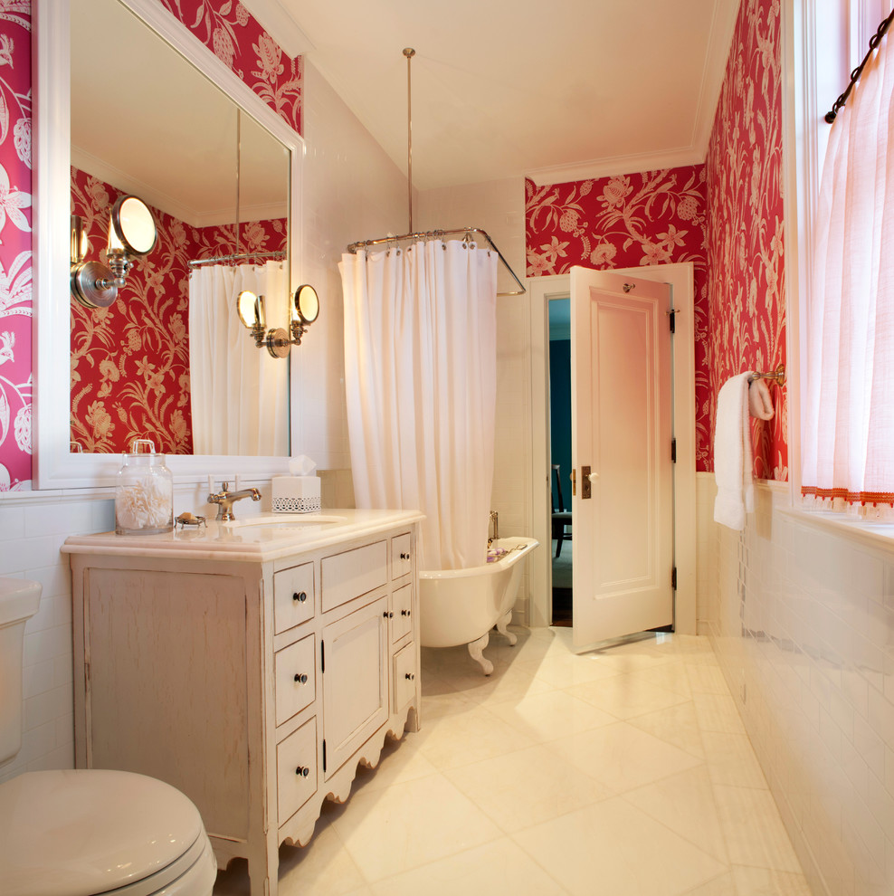 Bild på ett vintage vit vitt badrum, med vita skåp, ett badkar med tassar, en dusch/badkar-kombination, en toalettstol med separat cisternkåpa, vit kakel, keramikplattor, röda väggar, marmorgolv, ett undermonterad handfat, marmorbänkskiva och vitt golv