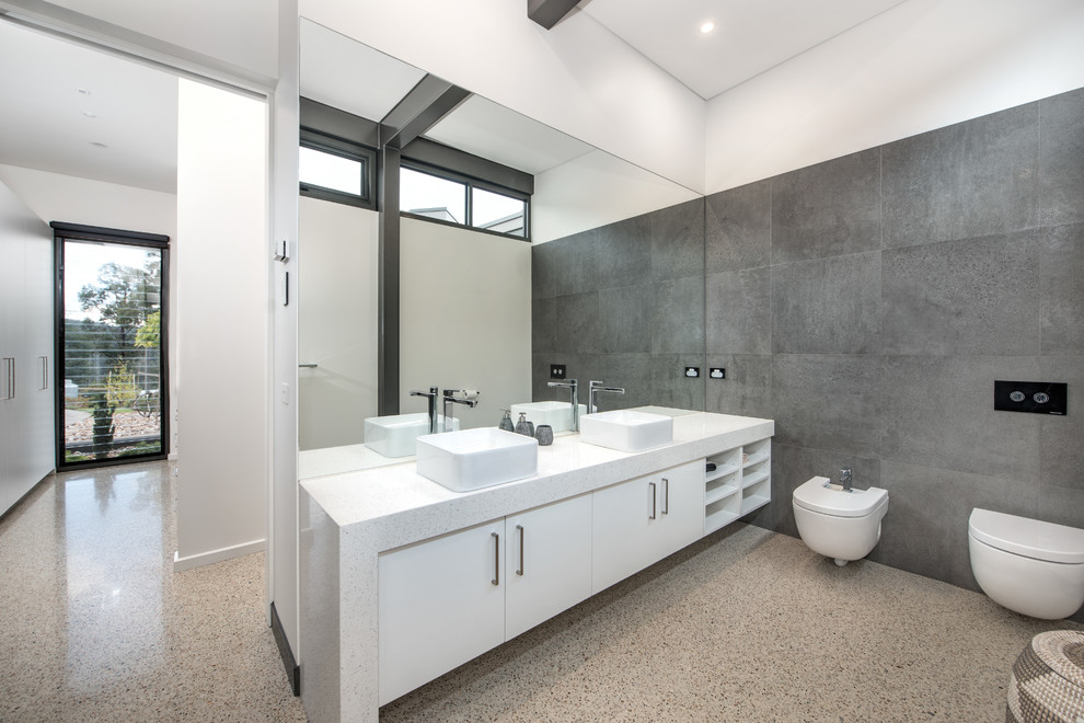 This is an example of an expansive contemporary ensuite bathroom in Melbourne with recessed-panel cabinets, white cabinets, a wall mounted toilet, grey tiles, grey walls, concrete flooring, a vessel sink and granite worktops.