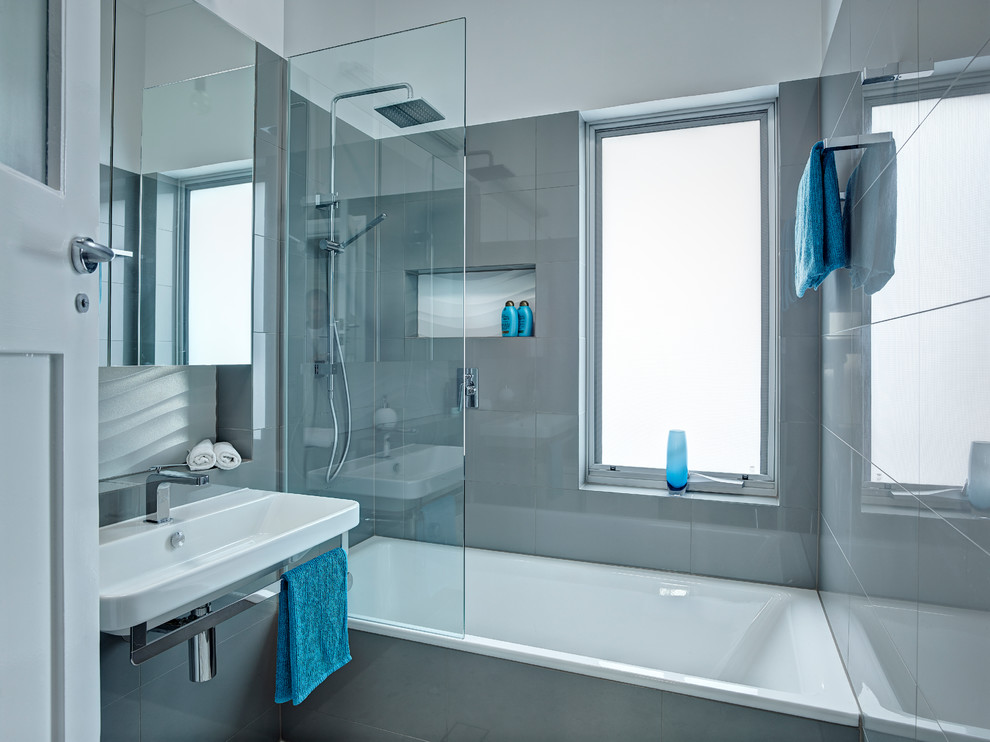 Small modern ensuite bathroom in Other with a wall-mounted sink, a built-in bath, a walk-in shower, a wall mounted toilet, grey tiles, grey walls and porcelain flooring.