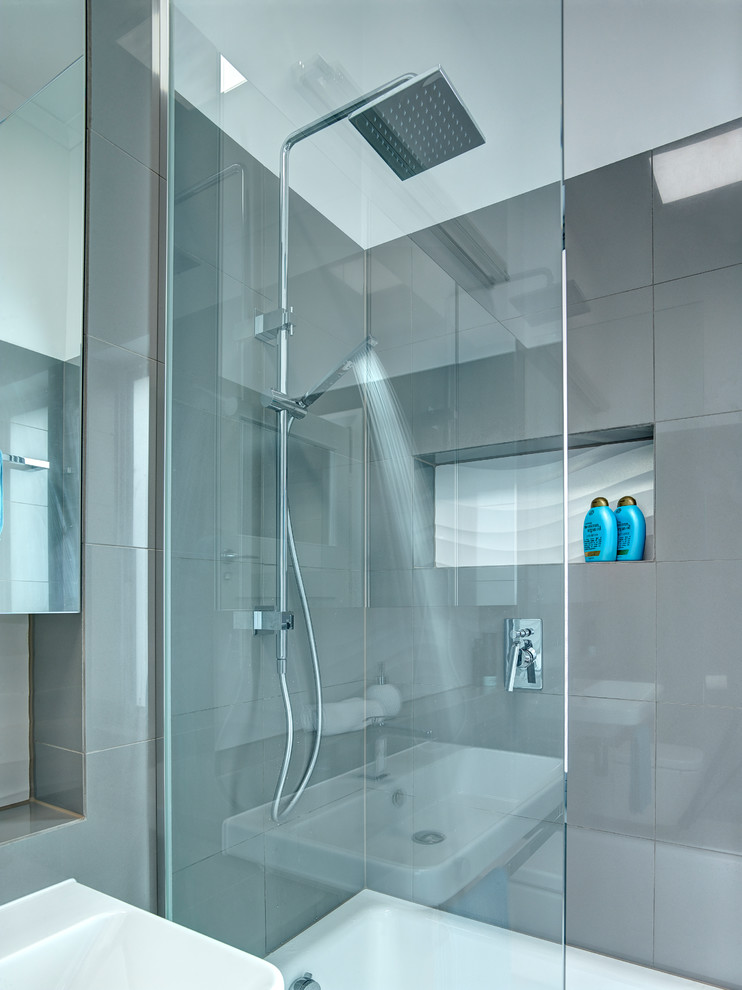 Foto de cuarto de baño principal minimalista pequeño con lavabo suspendido, bañera encastrada, ducha abierta, sanitario de pared, baldosas y/o azulejos grises, paredes grises y suelo de baldosas de porcelana