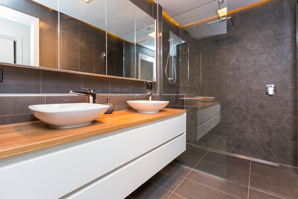 На фото: главная ванная комната среднего размера в стиле модернизм с белыми фасадами, столешницей из дерева, двойным душем, унитазом-моноблоком, серой плиткой, керамической плиткой и полом из керамической плитки с