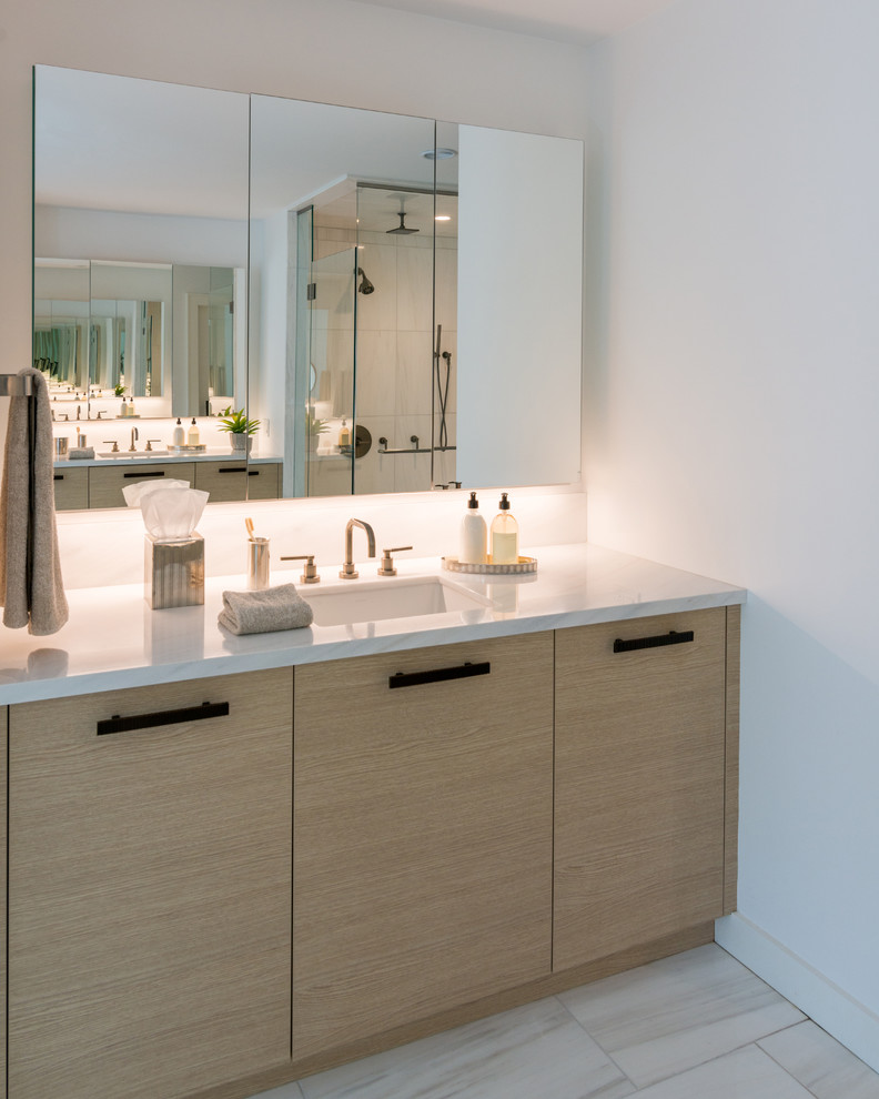 Large contemporary ensuite bathroom in New York with flat-panel cabinets, light wood cabinets, a freestanding bath, a corner shower, white walls, white floors, a hinged door, white worktops, limestone flooring, limestone worktops and a submerged sink.