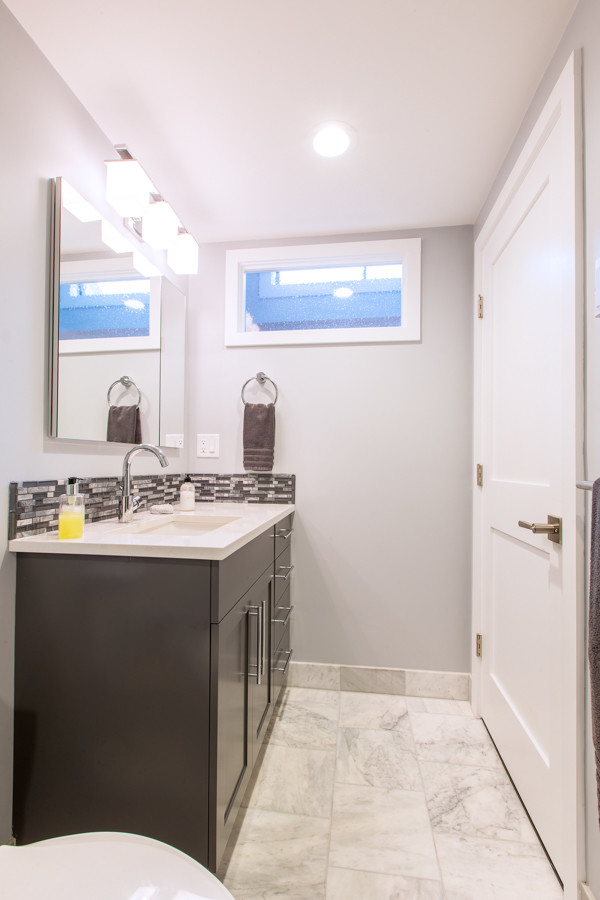 Imagen de cuarto de baño contemporáneo de tamaño medio con armarios con paneles lisos, puertas de armario de madera en tonos medios, ducha empotrada, sanitario de una pieza, baldosas y/o azulejos blancos, baldosas y/o azulejos de porcelana, paredes grises, suelo de mármol, aseo y ducha, lavabo bajoencimera y encimera de cuarzo compacto