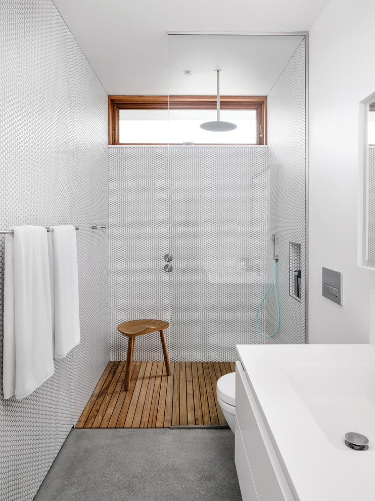 Foto på ett funkis vit badrum, med en öppen dusch, en vägghängd toalettstol, vit kakel, porslinskakel, vita väggar, betonggolv, ett integrerad handfat, grått golv och med dusch som är öppen