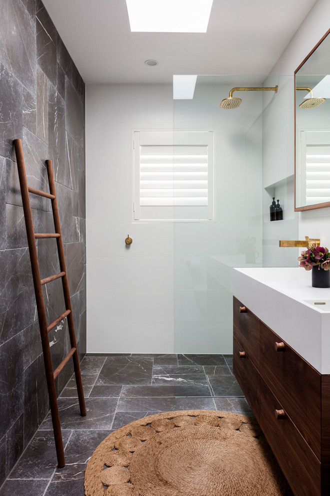 Mid-sized trendy 3/4 white tile and ceramic tile limestone floor and gray floor bathroom photo in Sydney with furniture-like cabinets, dark wood cabinets, a wall-mount toilet, gray walls, an integrated sink and solid surface countertops