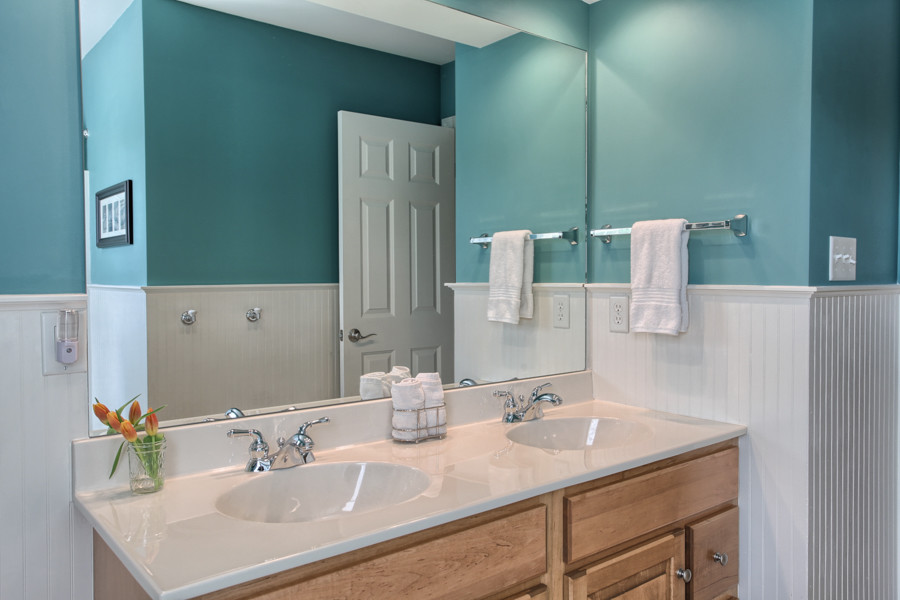 Diseño de cuarto de baño tradicional con armarios con paneles con relieve, puertas de armario de madera oscura, paredes azules, suelo de baldosas de porcelana, lavabo integrado y encimera de acrílico