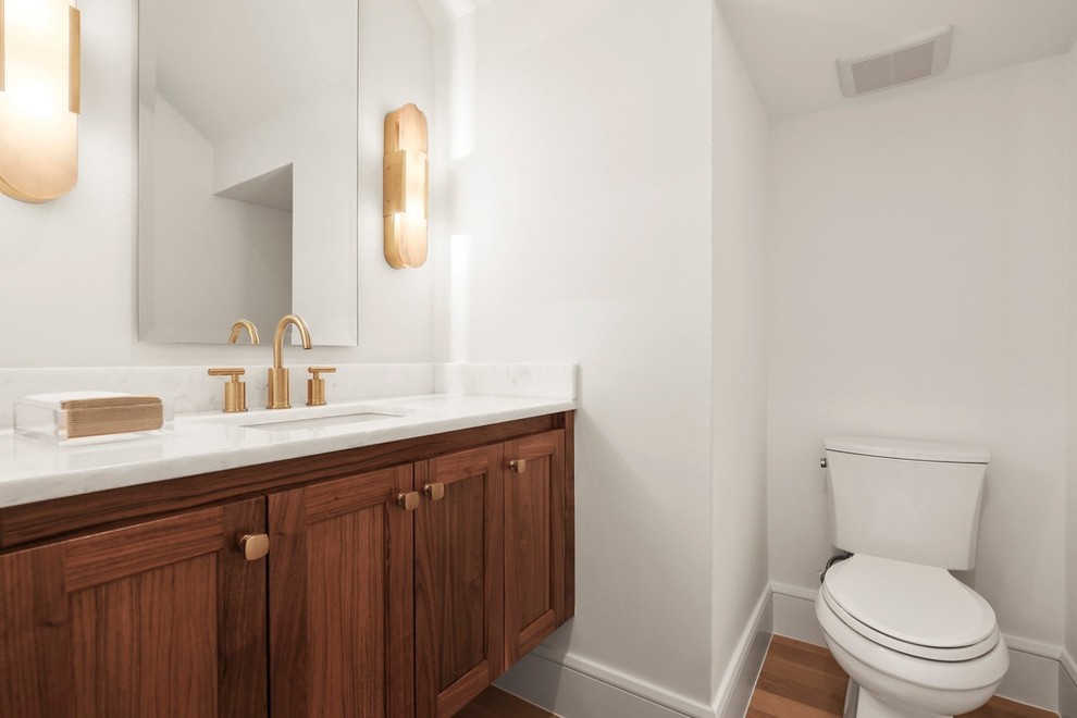 Mid-sized trendy 3/4 marble tile medium tone wood floor and brown floor bathroom photo in Other with shaker cabinets, dark wood cabinets, a two-piece toilet, white walls, an undermount sink, marble countertops and white countertops