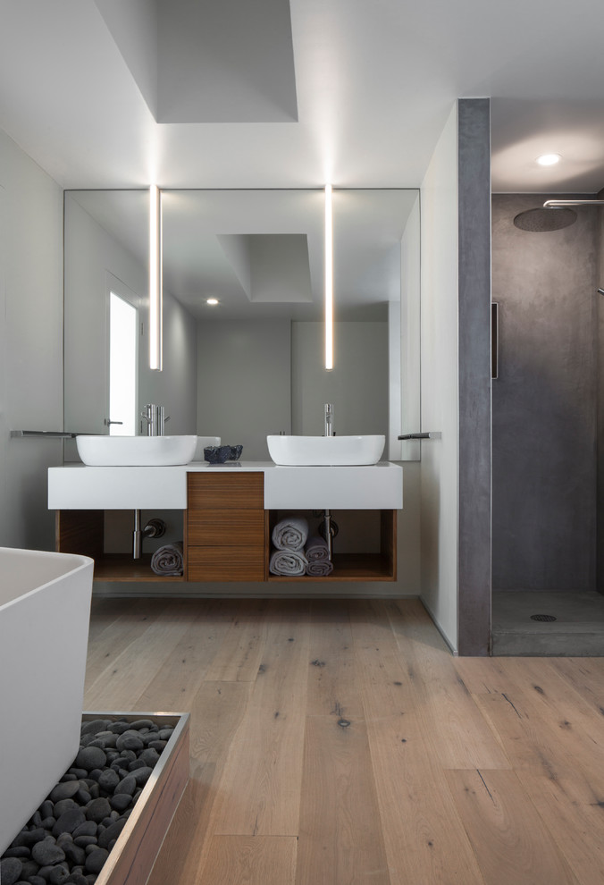 Photo of a modern bathroom in Los Angeles with flat-panel cabinets, medium wood cabinets, a freestanding bath, a corner shower, grey walls, light hardwood flooring, a vessel sink, beige floors and white worktops.