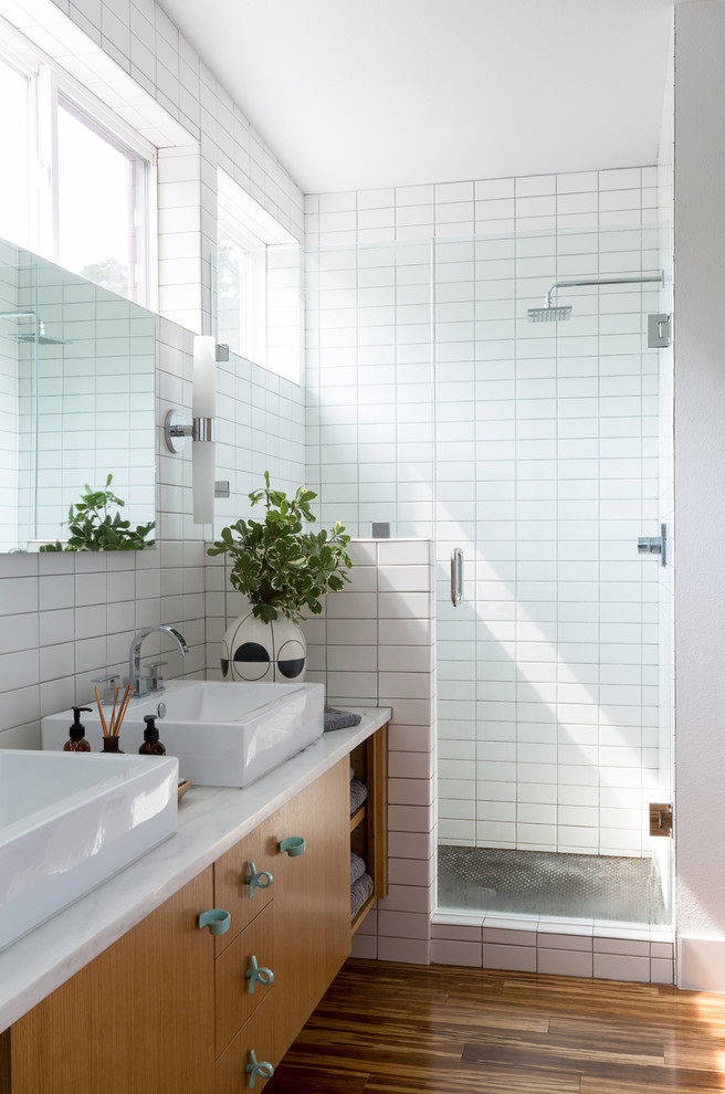 Inspiration for a midcentury shower room bathroom in Other with flat-panel cabinets, medium wood cabinets, a corner shower, white tiles, white walls, medium hardwood flooring, a vessel sink, brown floors and a hinged door.