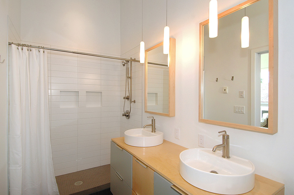 Modernes Badezimmer mit Aufsatzwaschbecken, flächenbündigen Schrankfronten, hellen Holzschränken, Laminat-Waschtisch, Duschnische, Toilette mit Aufsatzspülkasten, weißen Fliesen, Metrofliesen, weißer Wandfarbe und Keramikboden in Minneapolis