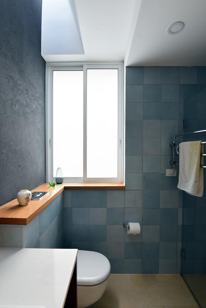 Réalisation d'une salle de bain principale design de taille moyenne avec WC suspendus, un carrelage bleu, des carreaux de céramique, un mur bleu, un sol en travertin et un plan de toilette en marbre.