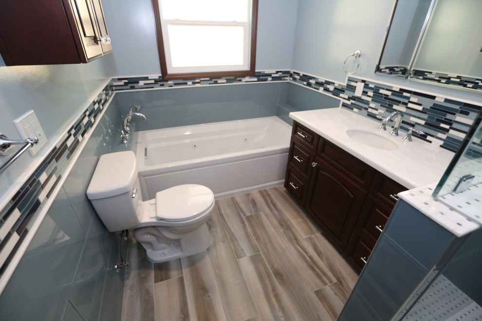 Cette photo montre une douche en alcôve principale moderne en bois foncé de taille moyenne avec un placard avec porte à panneau surélevé, une baignoire en alcôve, WC à poser, un carrelage bleu, un carrelage en pâte de verre, un mur bleu, un sol en carrelage de porcelaine, un lavabo encastré, un plan de toilette en marbre, un sol bleu, une cabine de douche à porte battante, un plan de toilette blanc, un banc de douche, meuble simple vasque et meuble-lavabo encastré.