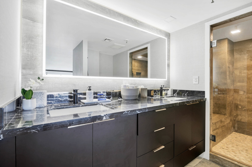 Example of a mid-sized trendy master beige tile, brown tile and porcelain tile marble floor and white floor alcove shower design in Miami with flat-panel cabinets, black cabinets, a one-piece toilet, gray walls, an undermount sink, onyx countertops, a hinged shower door and black countertops