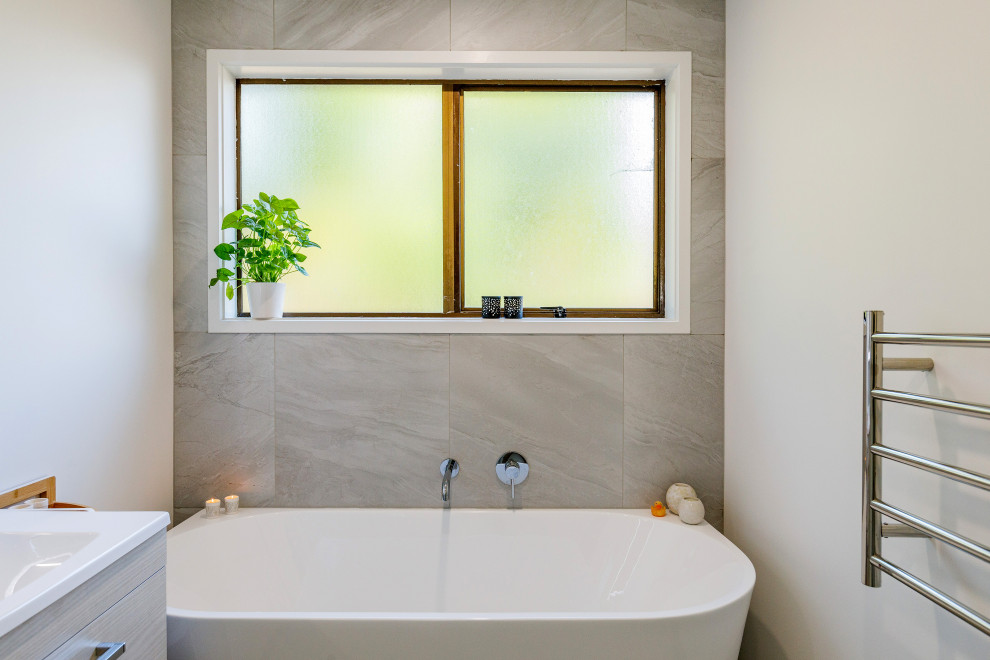 Источник вдохновения для домашнего уюта: маленькая ванная комната в современном стиле с светлыми деревянными фасадами, угловым душем, серой плиткой, керамогранитной плиткой, белыми стенами, полом из керамогранита, столешницей из искусственного камня, серым полом, душем с раздвижными дверями, белой столешницей, тумбой под одну раковину и подвесной тумбой для на участке и в саду