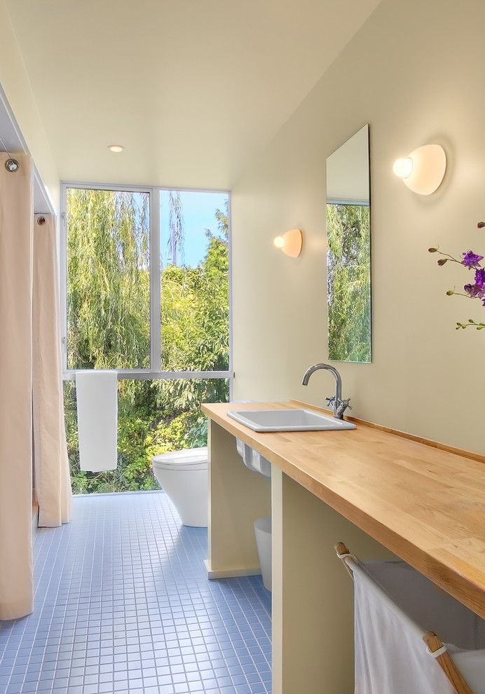 На фото: узкая и длинная ванная комната в современном стиле с накладной раковиной, открытыми фасадами, столешницей из дерева и синей плиткой