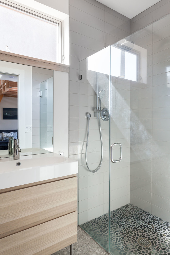 Cette image montre une petite salle de bain principale design en bois clair avec un placard à porte plane, une douche à l'italienne, WC séparés, un carrelage gris, des carreaux de porcelaine, un mur gris, un sol en galet, un lavabo intégré et un plan de toilette en surface solide.