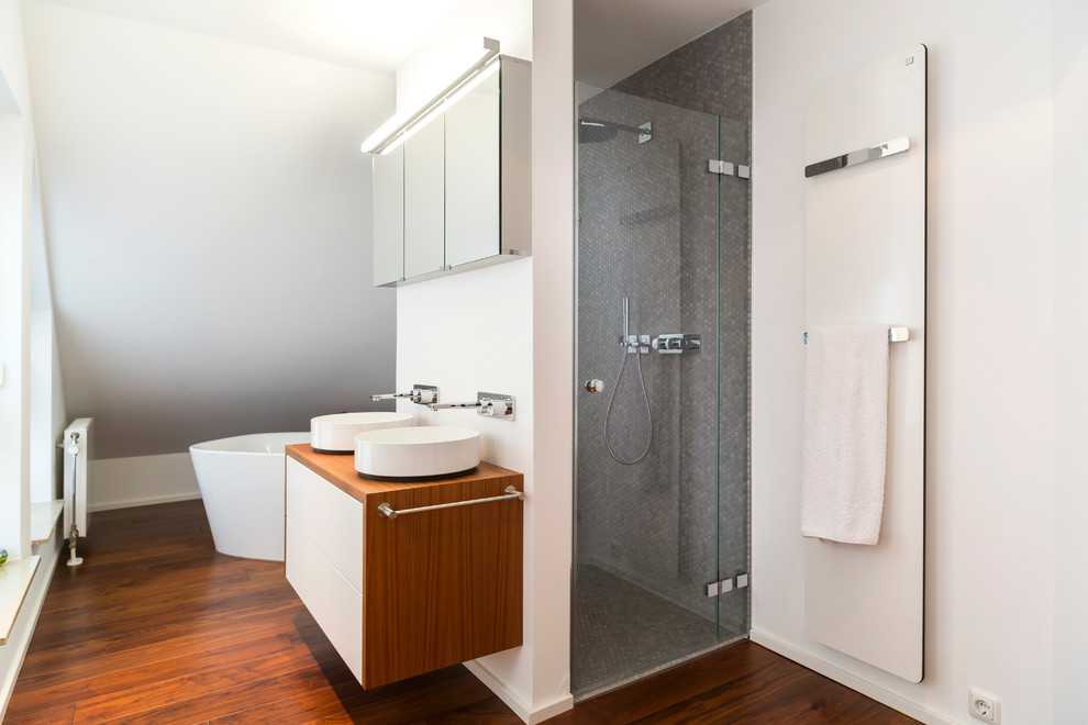 Exemple d'une grande douche en alcôve tendance avec un placard à porte plane, des portes de placard blanches, une baignoire indépendante, un carrelage gris, un mur blanc, parquet foncé, une vasque, un plan de toilette en bois, mosaïque et un plan de toilette marron.