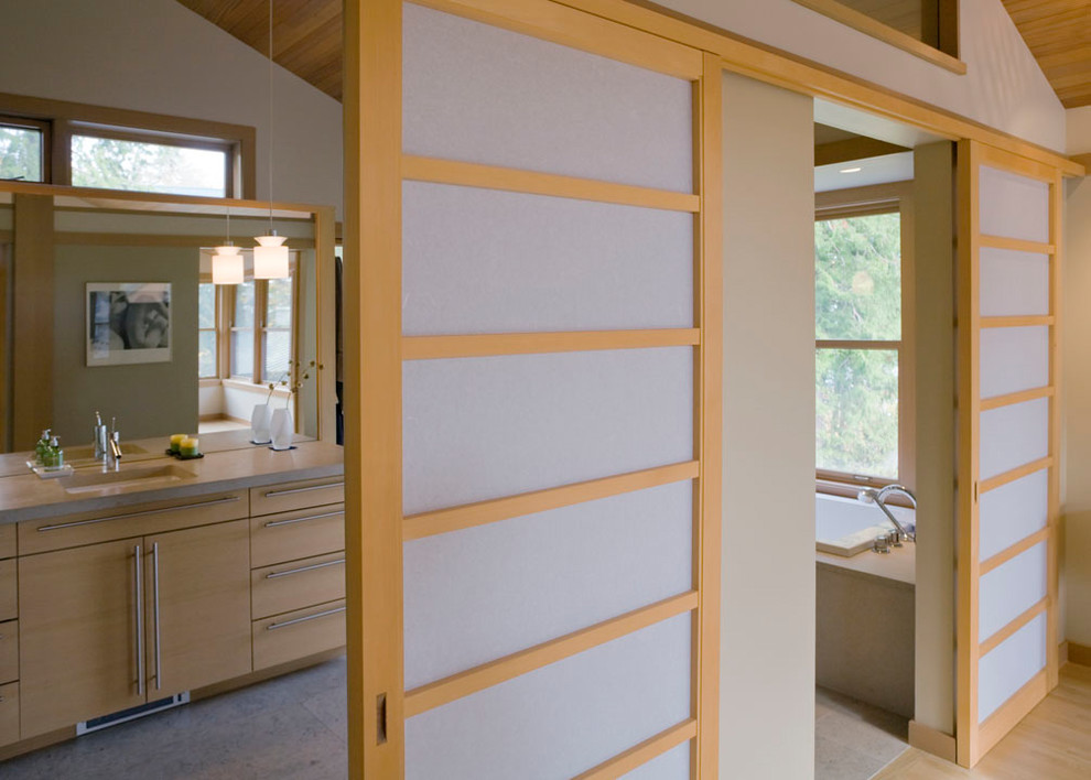 Aménagement d'une grande salle de bain principale asiatique en bois clair avec un placard à porte plane, une baignoire posée, un mur beige, un lavabo encastré, un plan de toilette en surface solide et un sol gris.