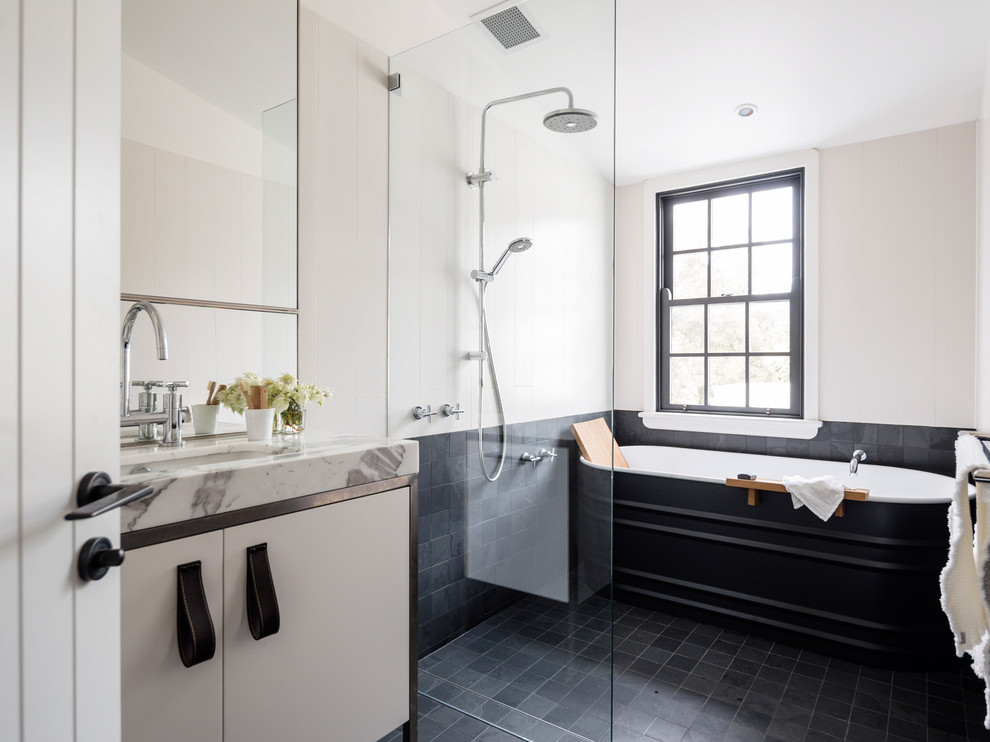 Photo of a contemporary ensuite bathroom in Sydney with a submerged sink, flat-panel cabinets, a freestanding bath, black tiles, beige walls, a built-in shower and white cabinets.