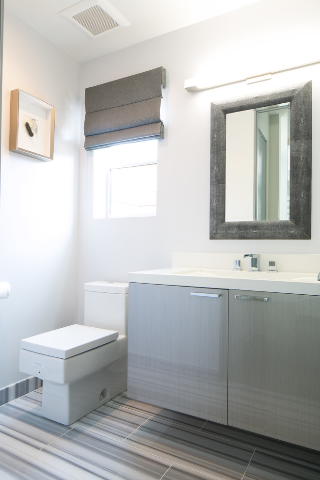 Modelo de cuarto de baño contemporáneo de tamaño medio con armarios con paneles lisos, puertas de armario grises, sanitario de una pieza, baldosas y/o azulejos blancos, paredes blancas, aseo y ducha y lavabo integrado