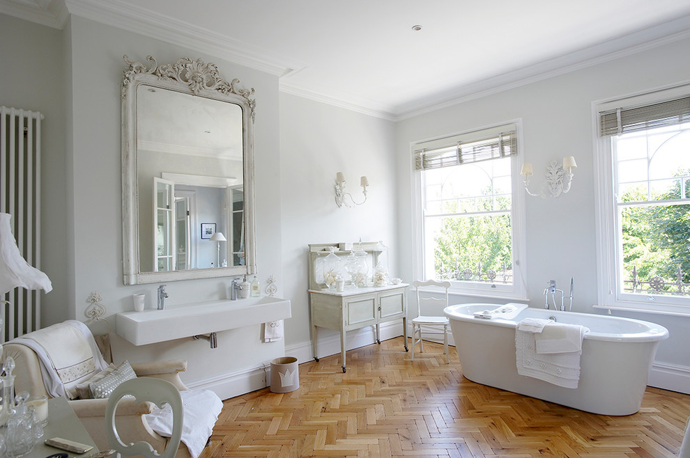 ロンドンにある広いヴィクトリアン調のおしゃれなマスターバスルーム (置き型浴槽、グレーの壁、ベージュのキャビネット、無垢フローリング、横長型シンク、白い洗面カウンター) の写真
