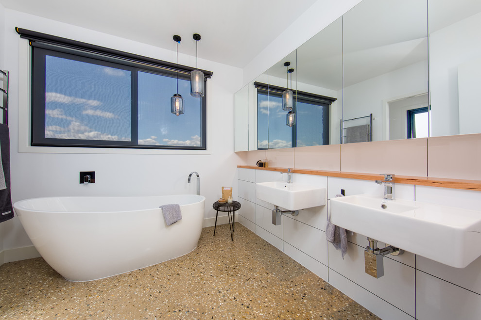 Ejemplo de cuarto de baño minimalista con bañera exenta, baldosas y/o azulejos blancos, suelo de cemento y lavabo suspendido