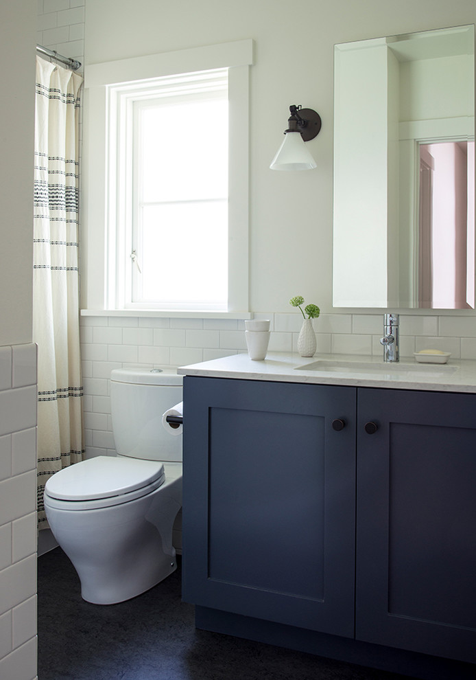 Photo of a medium sized classic family bathroom in Seattle with shaker cabinets, blue cabinets, an alcove bath, a two-piece toilet, ceramic tiles, white walls, lino flooring, a submerged sink, engineered stone worktops, black floors, a shower curtain, white worktops and white tiles.