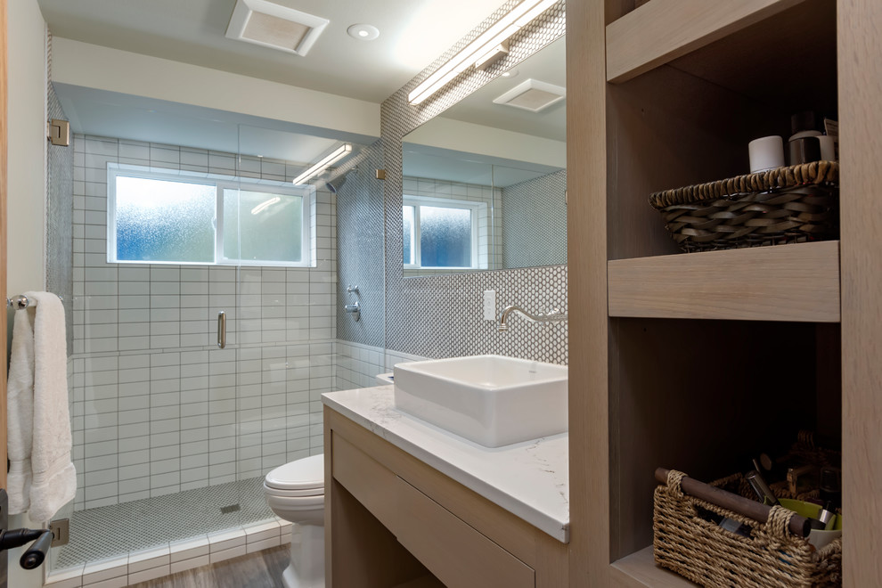 Inredning av ett klassiskt mellanstort badrum med dusch, med en toalettstol med hel cisternkåpa, klinkergolv i porslin, ett fristående handfat, öppna hyllor, skåp i ljust trä, vit kakel, tunnelbanekakel, grå väggar, bänkskiva i kvarts och brunt golv