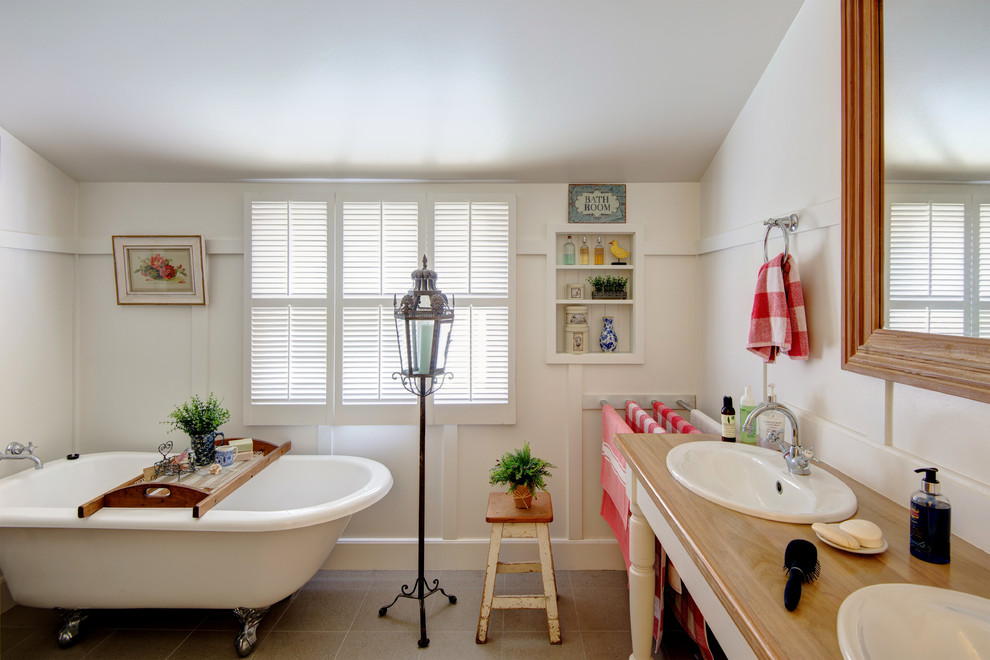 Modelo de cuarto de baño bohemio con lavabo encastrado, encimera de madera, bañera con patas y paredes blancas
