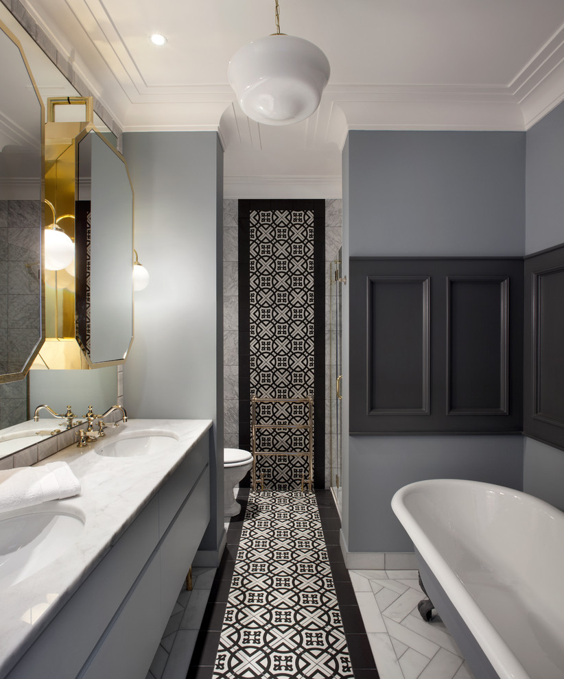 Cette image montre une salle de bain principale traditionnelle avec un placard à porte plane, des portes de placard grises, une baignoire sur pieds, un carrelage noir et blanc, un mur gris, un lavabo encastré et du carrelage bicolore.