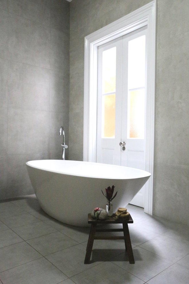 Inspiration pour une grande salle de bain minimaliste pour enfant avec une baignoire indépendante, un carrelage gris, des carreaux de porcelaine, un mur gris, un sol en carrelage de porcelaine et un sol gris.