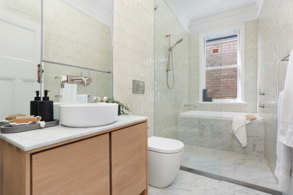 Cette image montre une salle de bain design en bois clair avec un placard à porte plane, une baignoire en alcôve, un espace douche bain, un carrelage blanc, une vasque, un sol blanc, un plan de toilette blanc, meuble simple vasque et meuble-lavabo encastré.