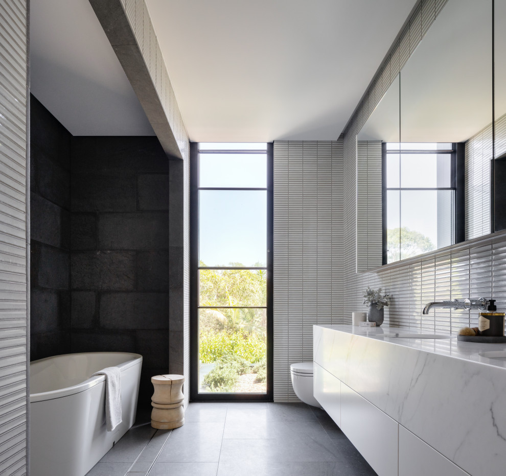 Idéer för stora funkis vitt en-suite badrum, med en öppen dusch, släta luckor, vita skåp, ett fristående badkar, en vägghängd toalettstol, svart kakel, vit kakel, grå väggar, ett undermonterad handfat och grått golv