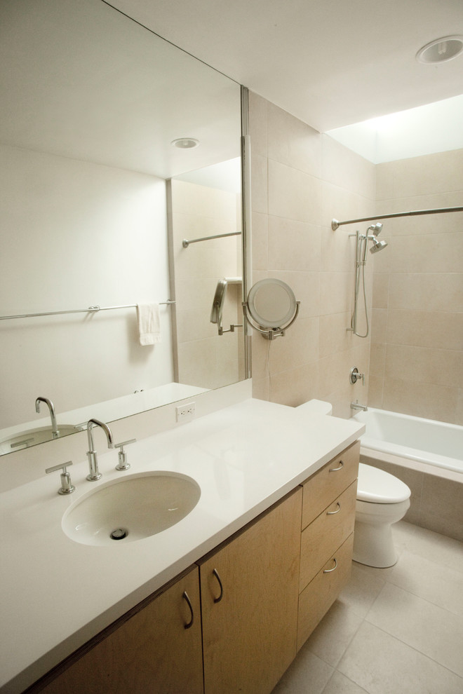 Foto på ett litet funkis en-suite badrum, med släta luckor, skåp i ljust trä, ett platsbyggt badkar, en dusch/badkar-kombination, en toalettstol med hel cisternkåpa, grå kakel, porslinskakel, vita väggar, klinkergolv i porslin, ett undermonterad handfat, bänkskiva i kvarts, grått golv och dusch med duschdraperi