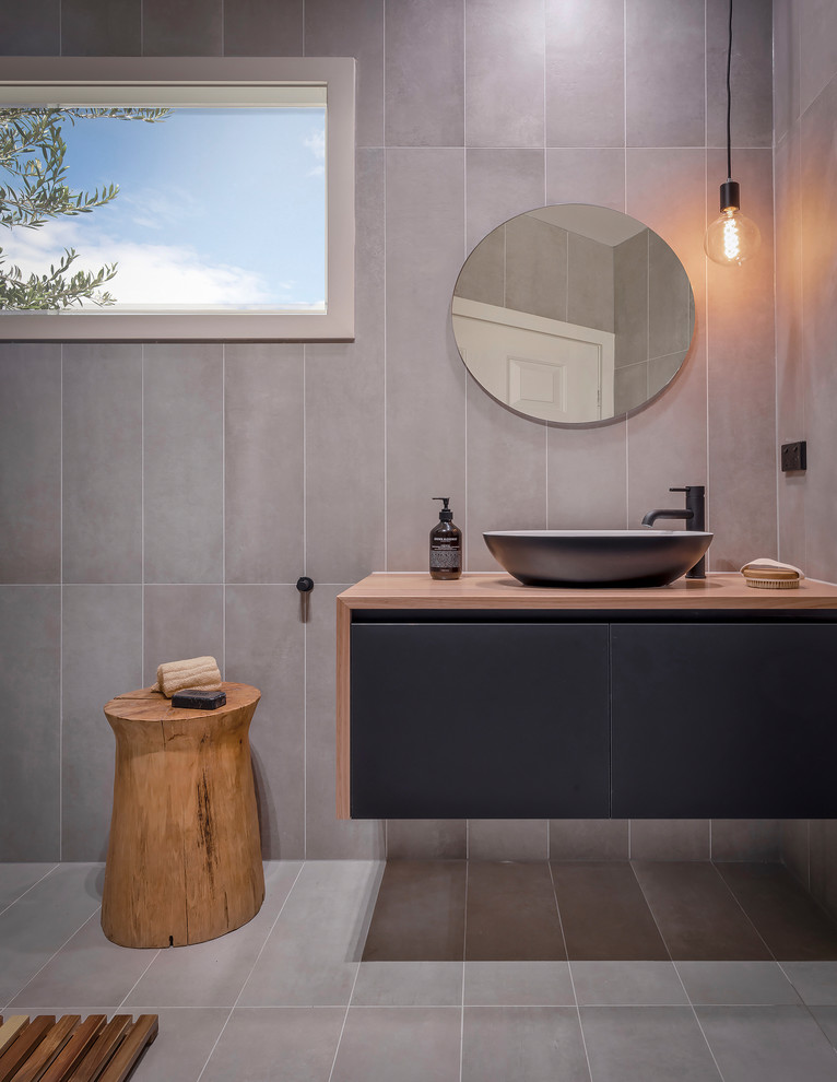 Inspiration för mellanstora moderna brunt badrum med dusch, med släta luckor, svarta skåp, en kantlös dusch, en vägghängd toalettstol, grå kakel, porslinskakel, grå väggar, klinkergolv i porslin, ett fristående handfat, träbänkskiva och grått golv