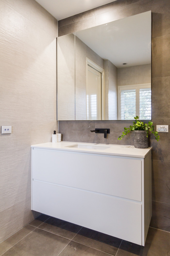 Photo of a medium sized modern family bathroom in Melbourne with flat-panel cabinets, white cabinets, a freestanding bath, grey tiles, porcelain tiles, white walls, porcelain flooring, a submerged sink, engineered stone worktops, grey floors and white worktops.