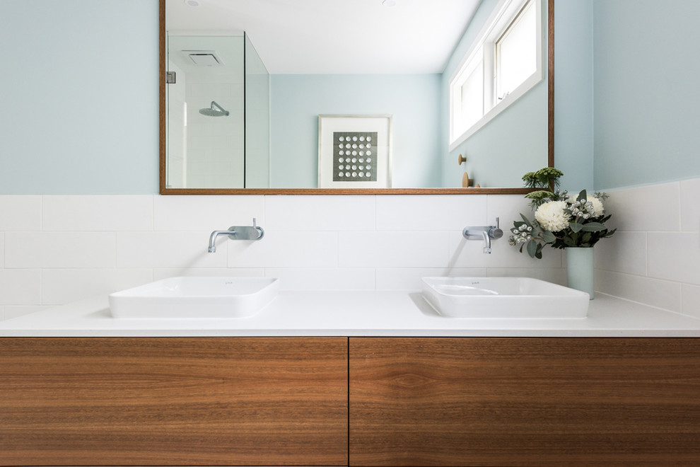 This is an example of a medium sized contemporary ensuite bathroom in Melbourne with flat-panel cabinets, medium wood cabinets, a freestanding bath, an alcove shower, a one-piece toilet, white tiles, porcelain tiles, blue walls, porcelain flooring, a built-in sink, engineered stone worktops, multi-coloured floors, a hinged door and white worktops.