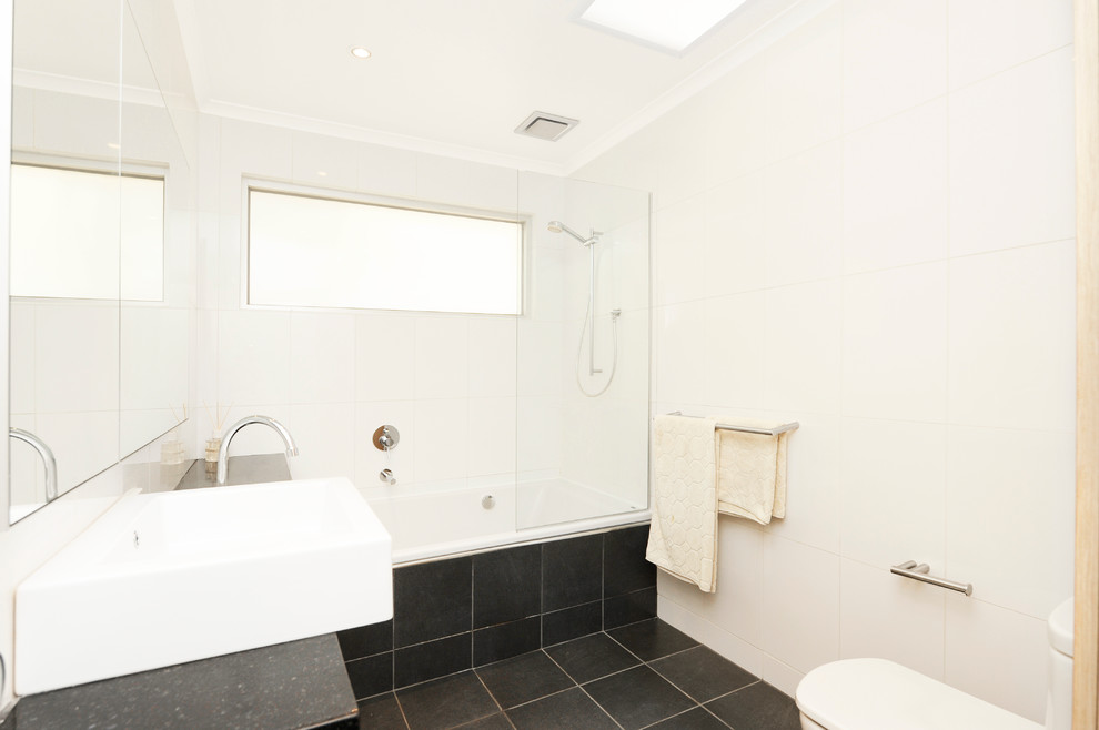 Idée de décoration pour une salle de bain minimaliste avec une baignoire en alcôve, un combiné douche/baignoire, WC suspendus, un carrelage blanc, un sol en carrelage de porcelaine, un sol noir, aucune cabine et un plan de toilette noir.
