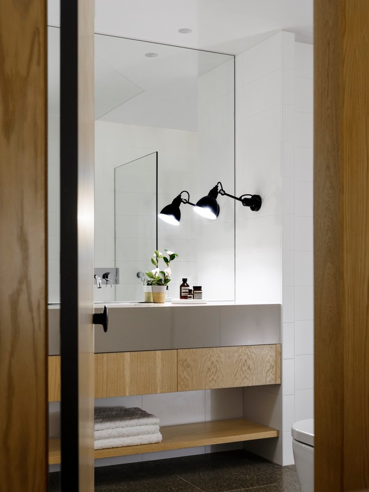 Imagen de cuarto de baño actual con armarios con paneles lisos, puertas de armario de madera clara, paredes blancas, lavabo bajoencimera, suelo negro y encimeras grises